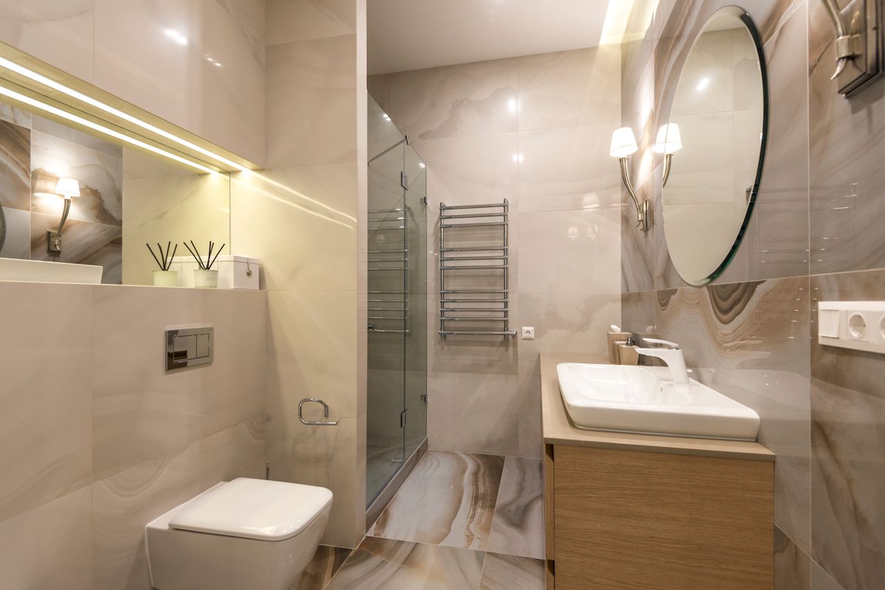 gallery-5 Elegant bathroom with marble tiles, large mirror, and modern fixtures.